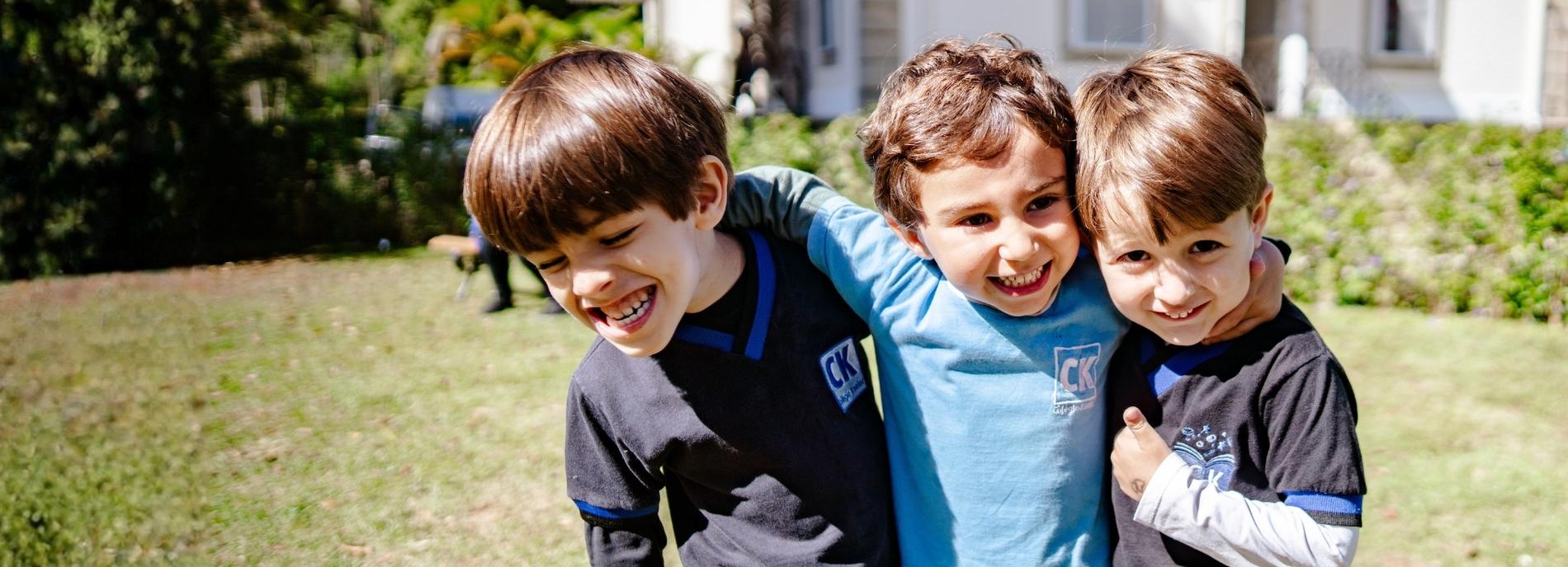 Três alunos do Colégio Koeler abraçados no jardim da escola